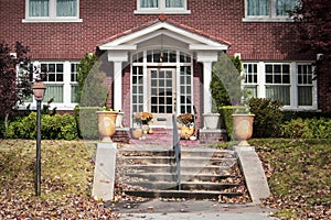 Entrance of two story upscale brick house in autumn with steps and pole laturn and pillared porch with attractive paned front door