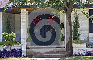 Entrance of an upscale white stone house with Asian style doors with large round handles and red wreaths and attractive landscapin