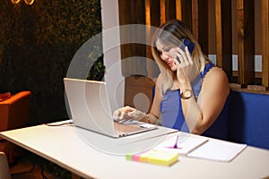 Entrepeneur woman talking on phone with a laptop taking notes