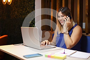 Entrepeneur woman talking on phone smiling with a laptop writing