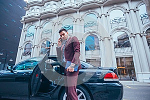 Entrepreneur Businessman standing in an urban area next to his limo while talking on the phone