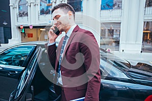 Entrepreneur Businessman standing in an urban area next to his limo while talking on the phone