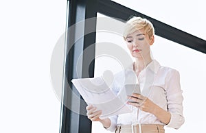 Entrepreneur Lady Using Smartphone Holding Papers Standing In Office, Low-Angle