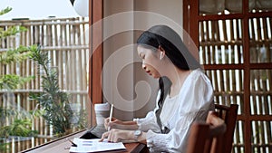 Entrepreneur working at cafe, diligently taking notes on her task using a tablet