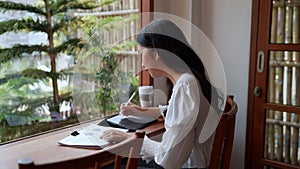 entrepreneur working at cafe, diligently taking notes on her task using a tablet