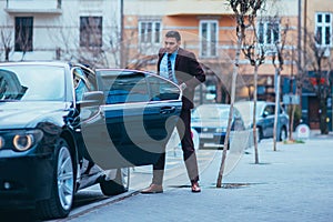 EntrepreneurBusinessman standing in an urban area and wearing a suit and tie next to his limo while talking on the phone