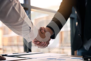 Entrepreneurs collaboration deal shaking hands in a modern office and financial paper graph on desk