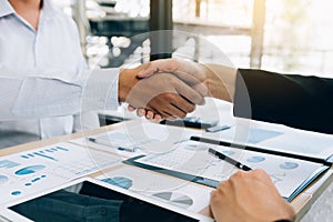 Entrepreneurs collaboration deal shaking hands in a modern office and financial paper graph on desk