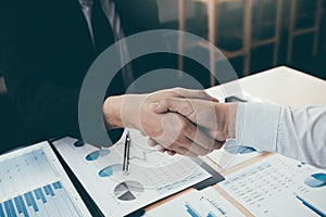 Entrepreneurs collaboration deal shaking hands in a modern office and financial paper graph on desk