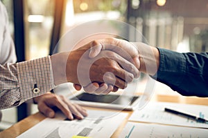 Entrepreneurs collaboration deal shaking hands in a modern office and financial paper graph on desk