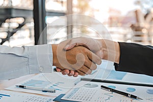 Entrepreneurs collaboration deal shaking hands in a modern office and financial paper graph on desk