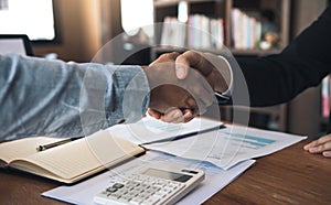 Entrepreneurs collaboration deal shaking hands in a modern office and financial paper graph on desk