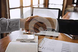 Entrepreneurs collaboration deal shaking hands in a modern office and financial paper graph on desk