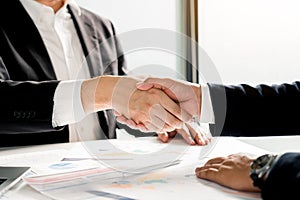 Entrepreneurs collaboration deal shaking hands in a modern office and financial paper graph on desk