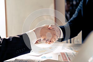 Entrepreneurs collaboration deal shaking hands in a modern office and financial paper graph on desk