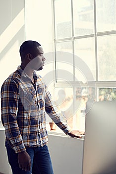 Entrepreneurs see possibility in everything. a young businessman looking thoughtfully out of a window in a modern office