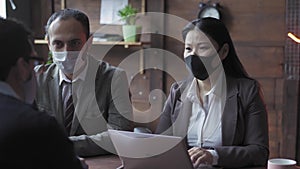 Entrepreneurs working in office wearing protective mask discussing work progress or problems during quarantine pandemic