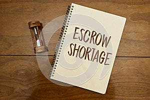 The entry Escrow shortage was made in a notebook with hourglass on wood table.