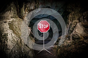 Entry to dark cave blocked with STOP sign.