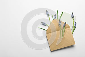 Envelope with beautiful spring muscari flowers and card on light background, flat lay