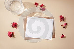 Envelope with blank card, red horse chestnut flowers and glass of water with harsh shadowson neutral beige background photo