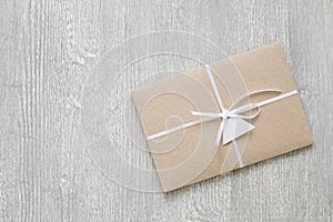 Envelope from brown craft paper decorated with ribbon and label on gray wooden background.