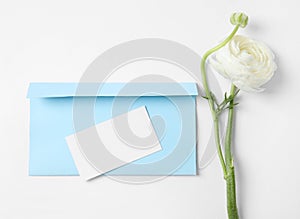 Envelope with card and beautiful ranunculus flower on white background, top view