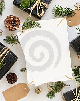 Envelope and card near Christmas decor, gift boxes and green fir branches top view, mockup