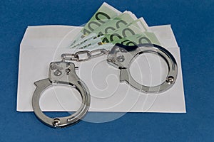 Envelope with euros on a blue background. Steel handcuffs on the envelope. Bribery concept. Punishment for wages in envelopes.