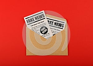Envelope with FAKE NEWS newspapers over red