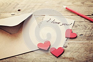 Envelope or letter, red hearts and notes I love you on vintage wooden table for Valentines Day in retro toning.