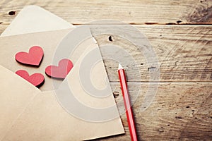 Envelope or letter and red hearts on rustic table for love message on Valentines Day in retro toning.