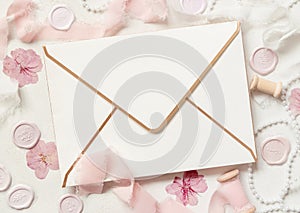 Envelope near pink decorations, seals and silk ribbons on white table top view, wedding mockup