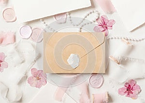 Envelope near pink decorations, seals and silk ribbons on white table top view, wedding mockup