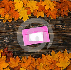 An envelope and paper with an empty space for text on a pile of bright autumn leaves against a dark wooden table