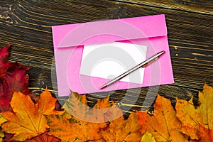 An envelope and paper with an empty space for text on a pile of bright autumn leaves against a dark wooden table