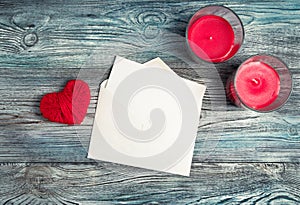 An envelope with a white letter, two candles and a red heart on a wooden background.