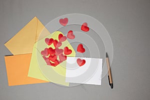 Envelopes and a white card for text with red falling hearts on a gray concrete background. Valentine's Day greeting