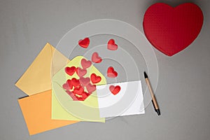 Envelopes and a white card for text with red falling hearts on a gray concrete background. Valentine's Day greeting