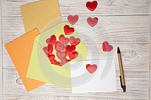Envelopes and a white card for text with red falling hearts on a white wooden background. Happy Valentine's Day