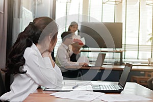 Envious angry Asian business woman looking affectionate couple in love in office with sunshine effect. Jealousy and envy in friend