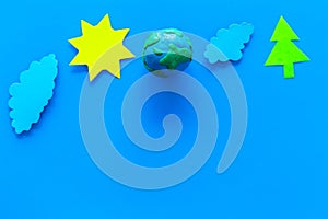 Environment protection concept. Plastiline symbol of planet Earth and sun, cloud, tree coutout on blue background top