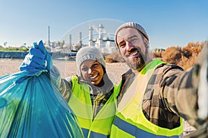 A environmental activist or volunteer multiracial couple picking up trash og the beatch, and taking a selfie portrait