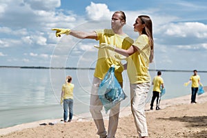 Environmental Activists. Two young man and woman holding trash bag and discussing something while cleaning beach area