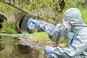 Environmental biologist in a protective suit and mask examines water from the river for viruses
