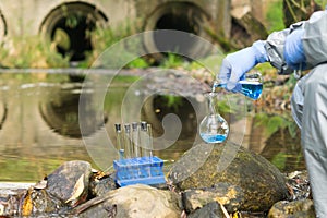 Environmental biologist in a protective suit on the shore of a reservoir conducts an express test of river water for pollution