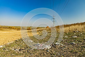 Environmental disaster garbage polluted field country side space summer time horizon background with power line high voltage wires