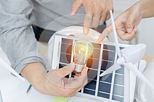 Environmental engineer holding and pointing light bulb in modern office with solar cell sample and wind turbine model