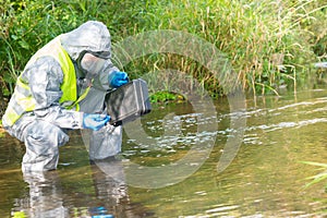 An environmental laboratory specialist in a protective suit and mask stands in the water and measures the level of pollution with