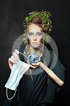 Environmental protection concept. Woman with used single-use face mask during COVID-19 and holding Earth